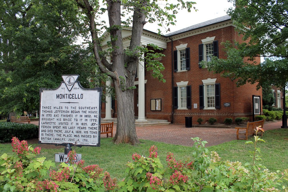 An historical building made of red brick with white columns at the entrance surrounded by trees.