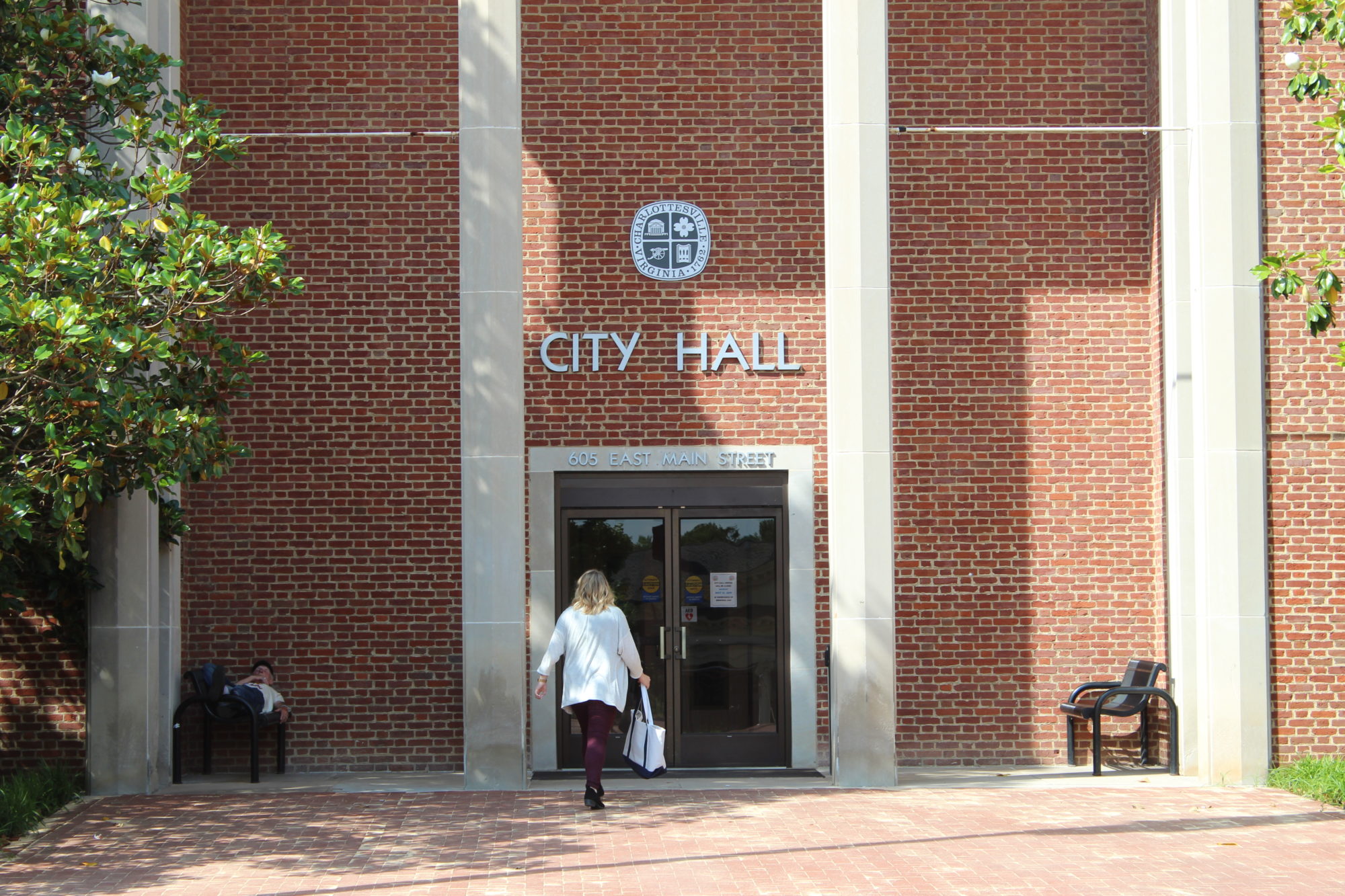 A person stands outside a brick building with columns. The building has text above the door that reads CITY HALL.