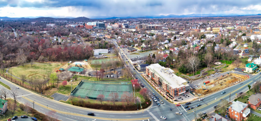 An aerial view of a street corner, showing tennis courts and buildings among trees