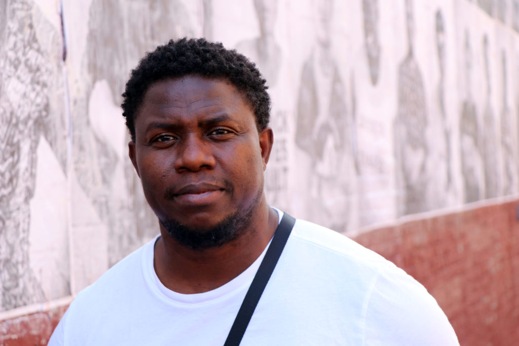 A man poses for a picture outside in front of a mural.