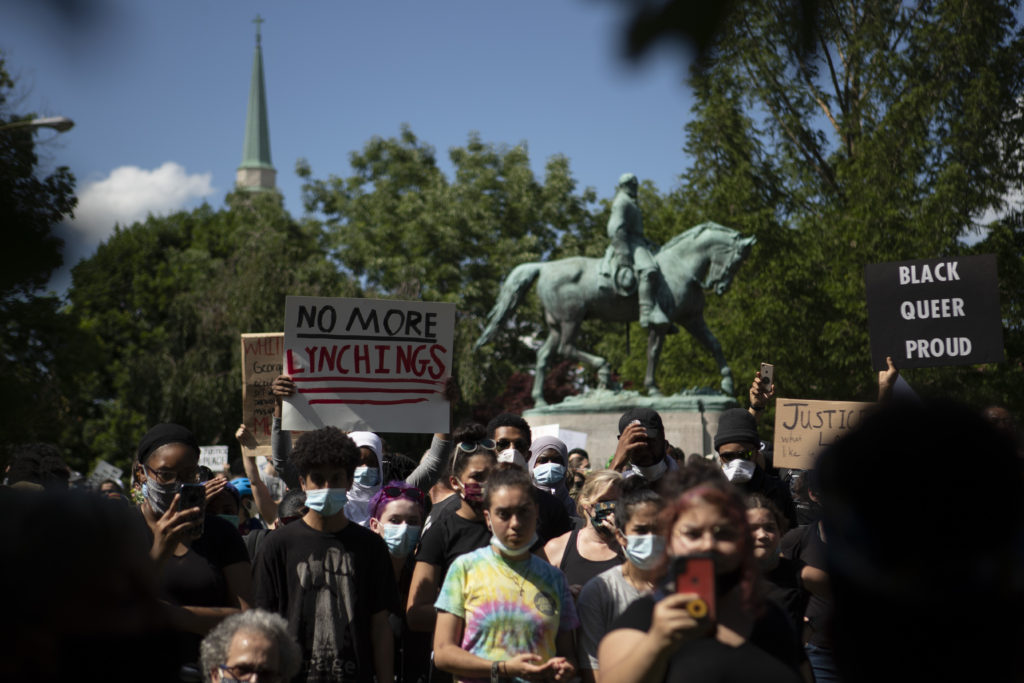 An crowd of people stand before a statue of a man on a horse