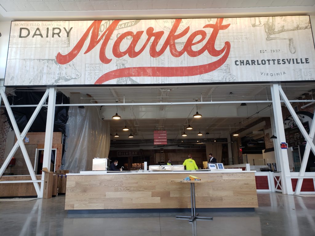 A large room in a building is pictured with a long counter. Above it is a sign that reads "Dairy Market."