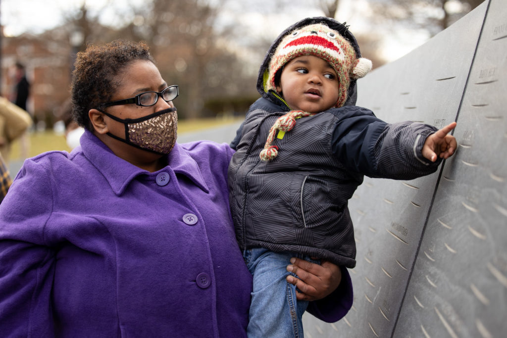 A woman holds a small child who is touching a wall