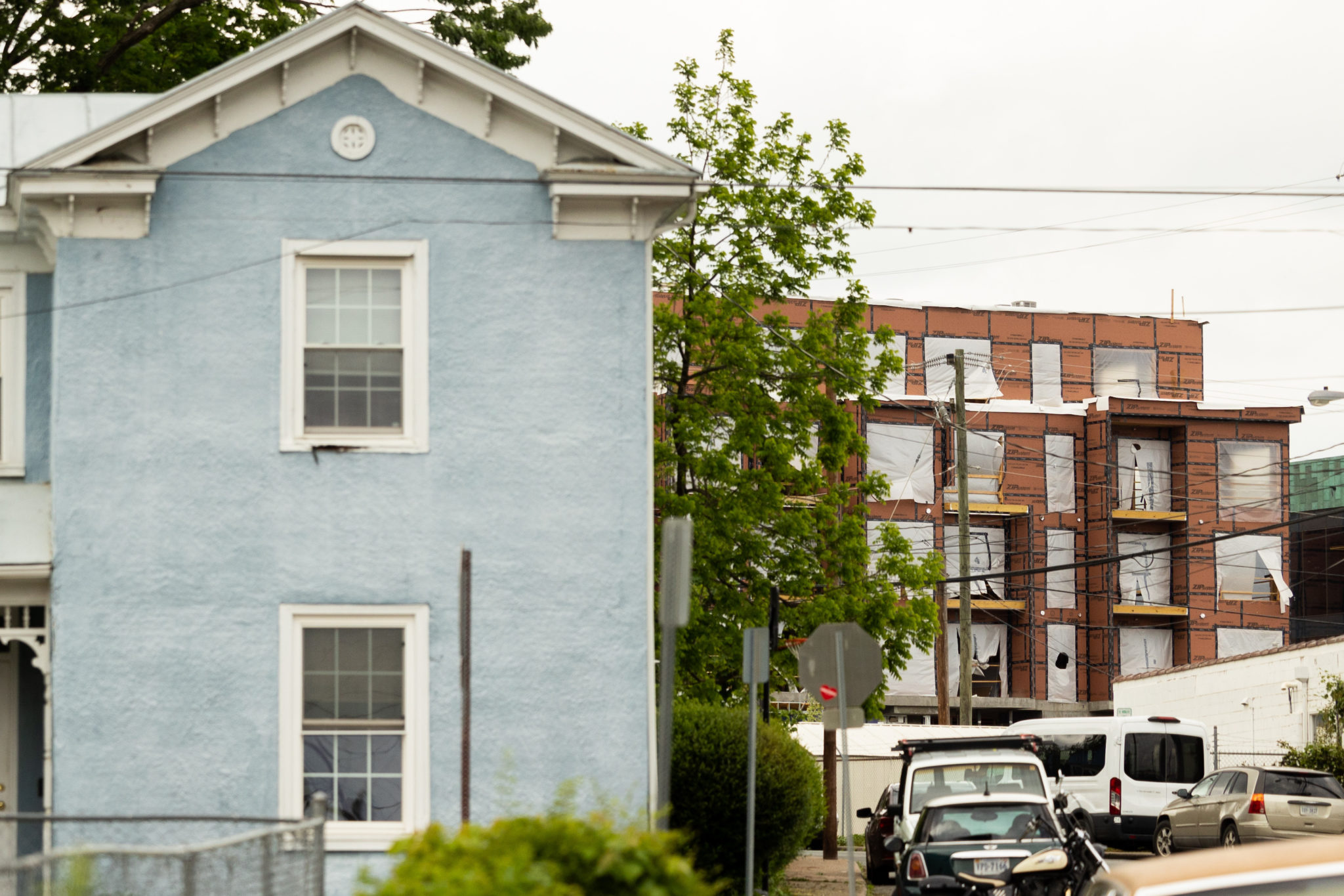 A blue two story house sits in the foreground in front of a multi-story apartment building.