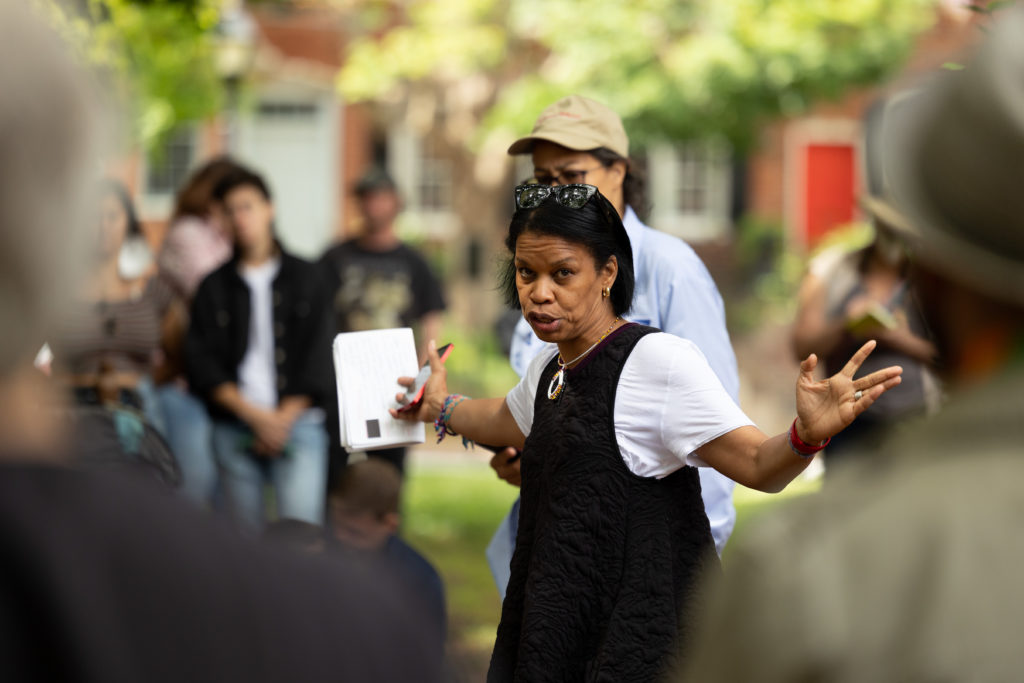 A woman with arms outstretched talks to a group of people