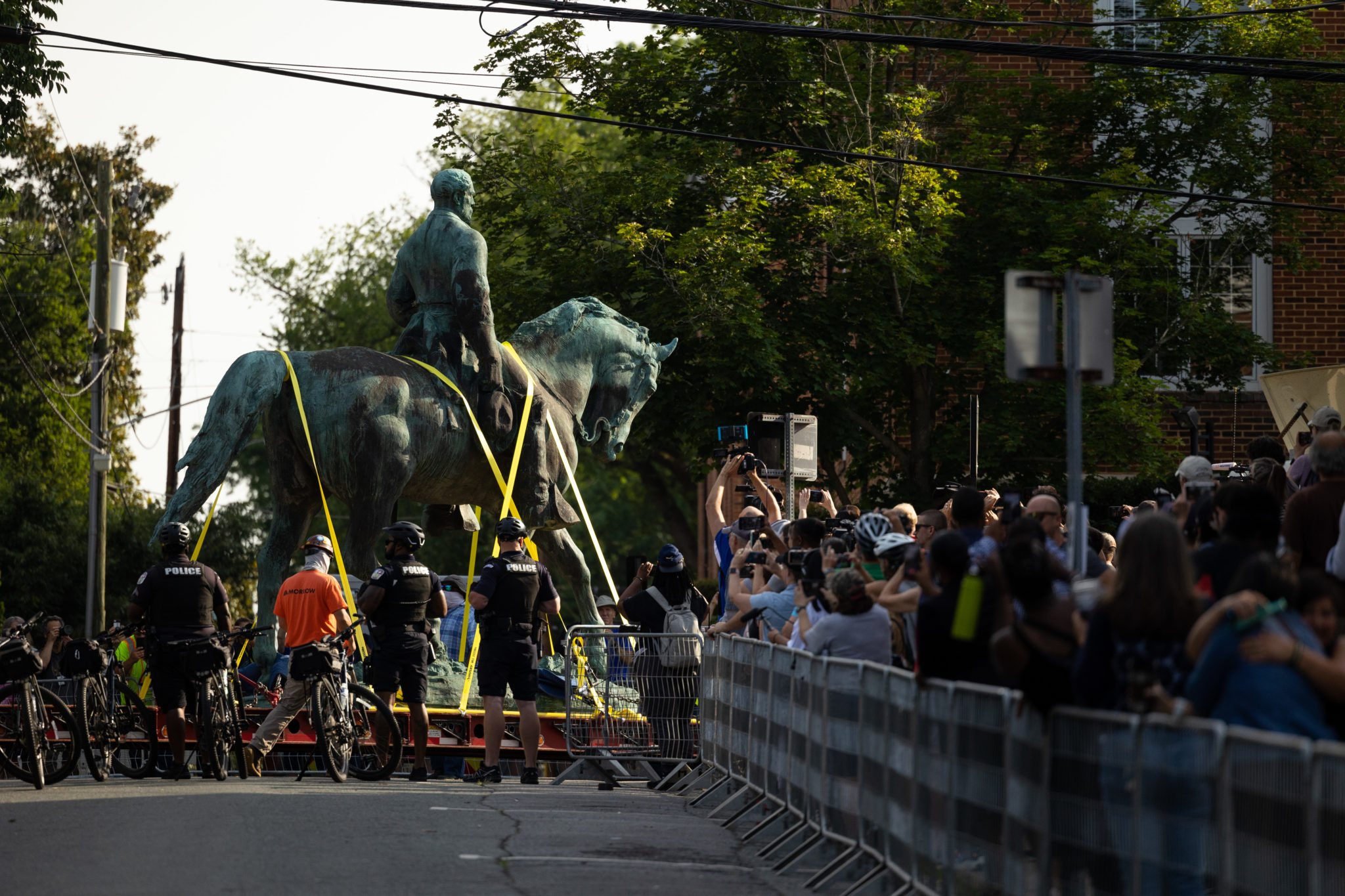 A large statue is being moved down the streets with onlookers behind barriers