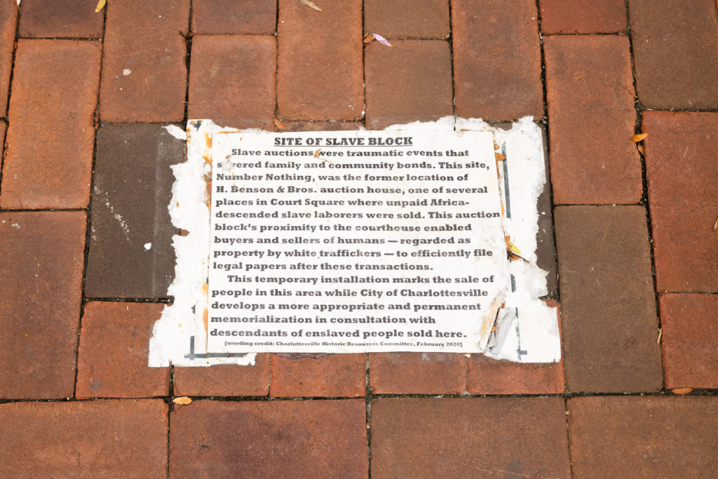 A piece of paper with printed writing on it is glued to a brick sidewalk.