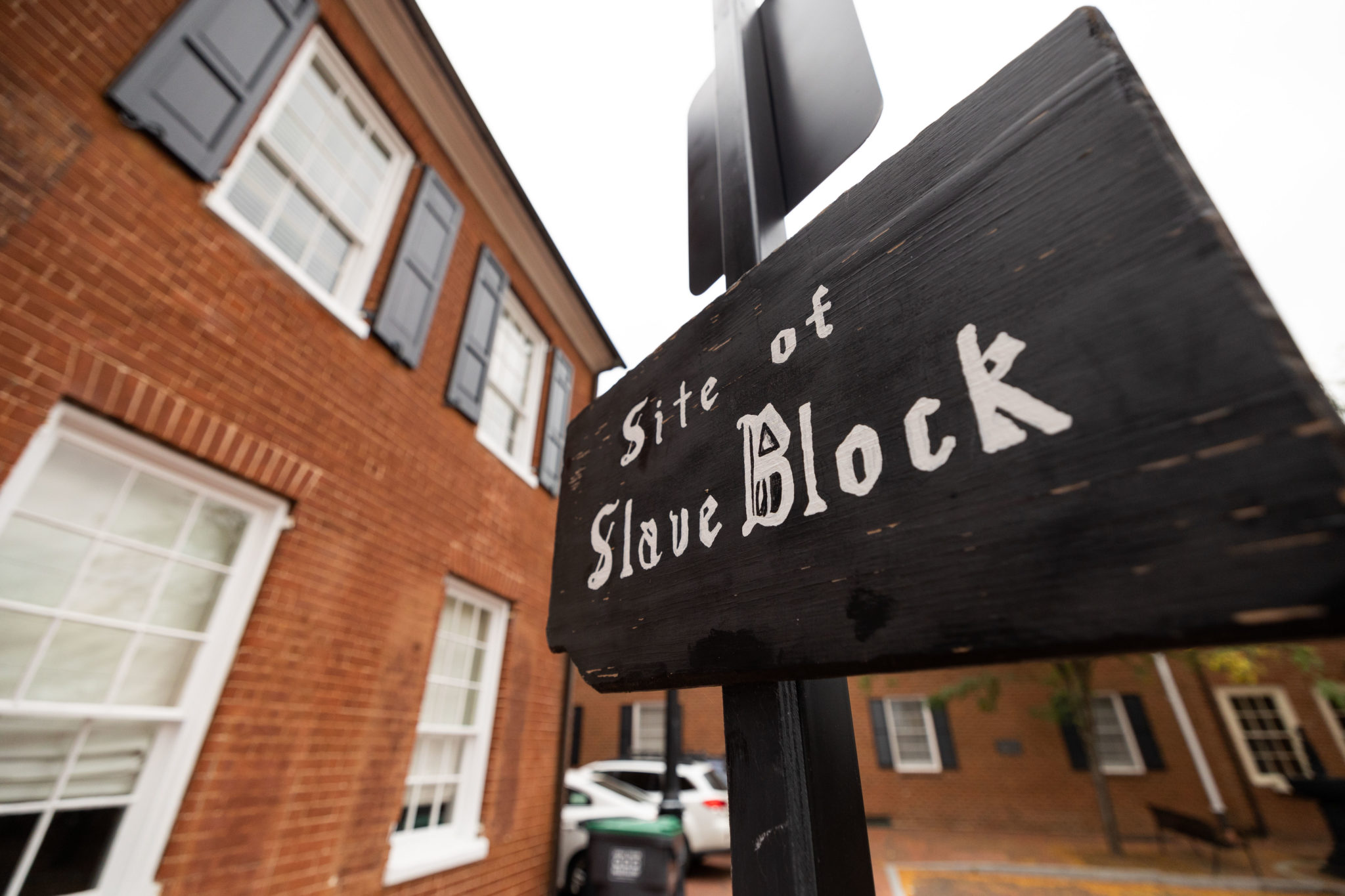 A black wooden sign with white block letters reads, "Site of Slave Block."