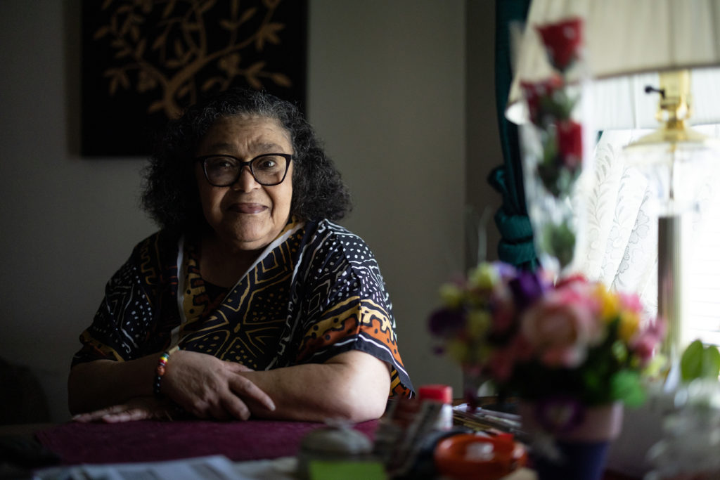 A woman in glasses next to a window, with a bouquet of flowers in the foreground.