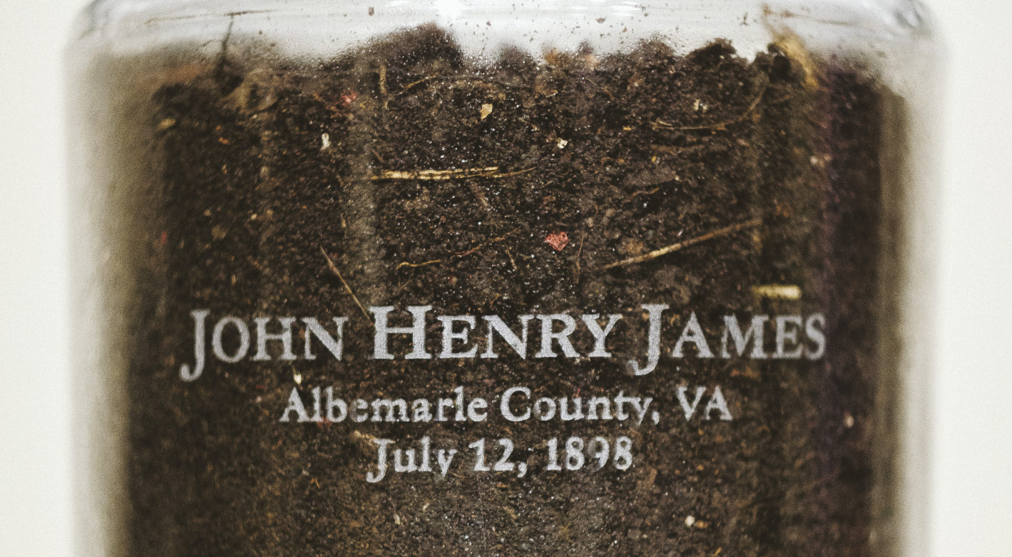 A close-up of a jar of soil with inscription "John Henry James Albemarle County, VA July 12, 1898"