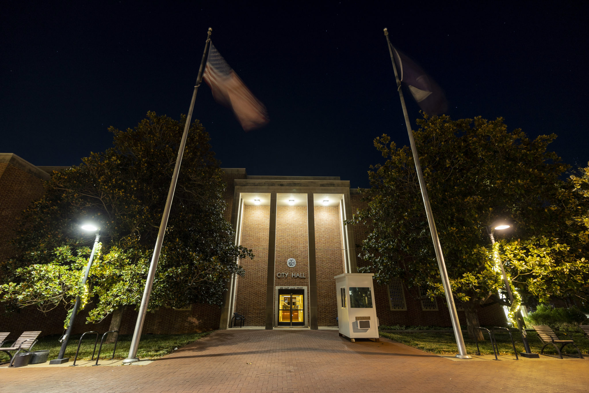 A photo of a brick building with the words City Hall on it, with flags in front