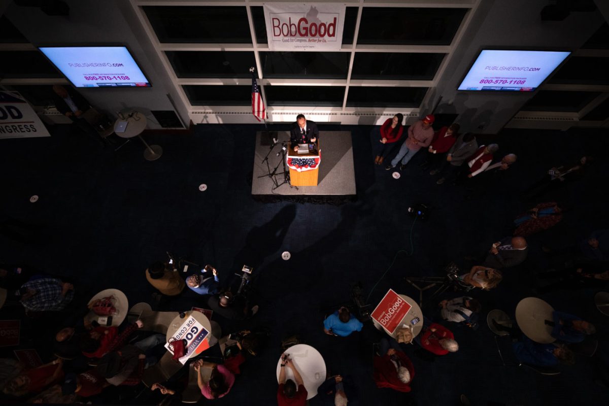 Photo shows a view from above of a man at a podium surrounded by people standing around tables. A sign behind the podium reads, “Bob Good.”