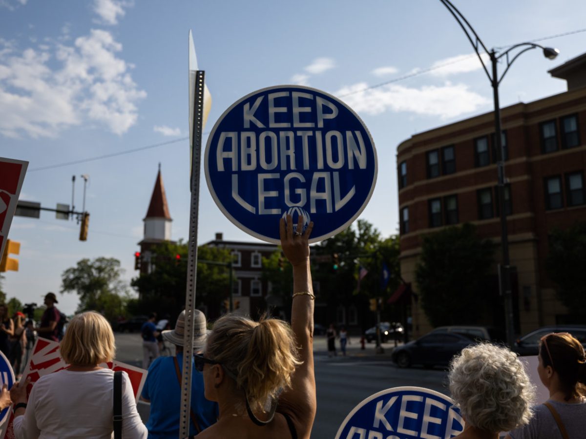 Women stand on the side of a street holding signs that read “Keep Abortion Legal.”
