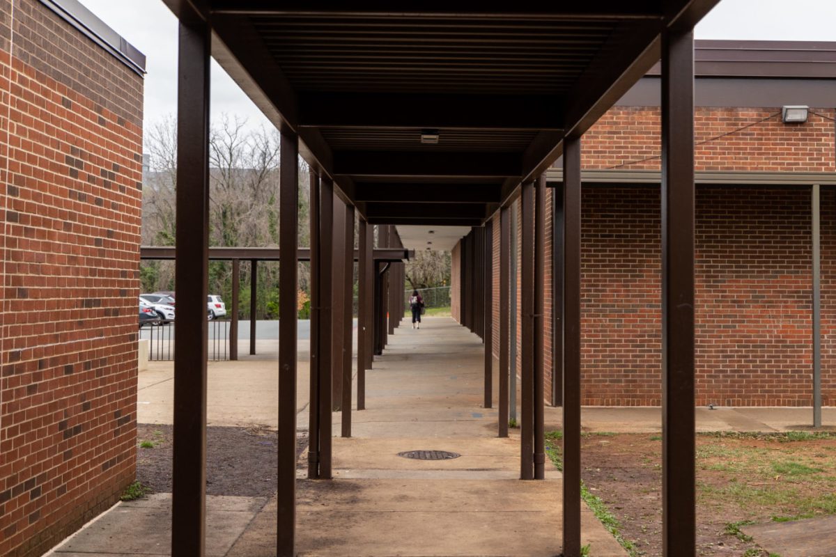 A student walks underneath a metal-covered concrete walkway between two brick buildings.