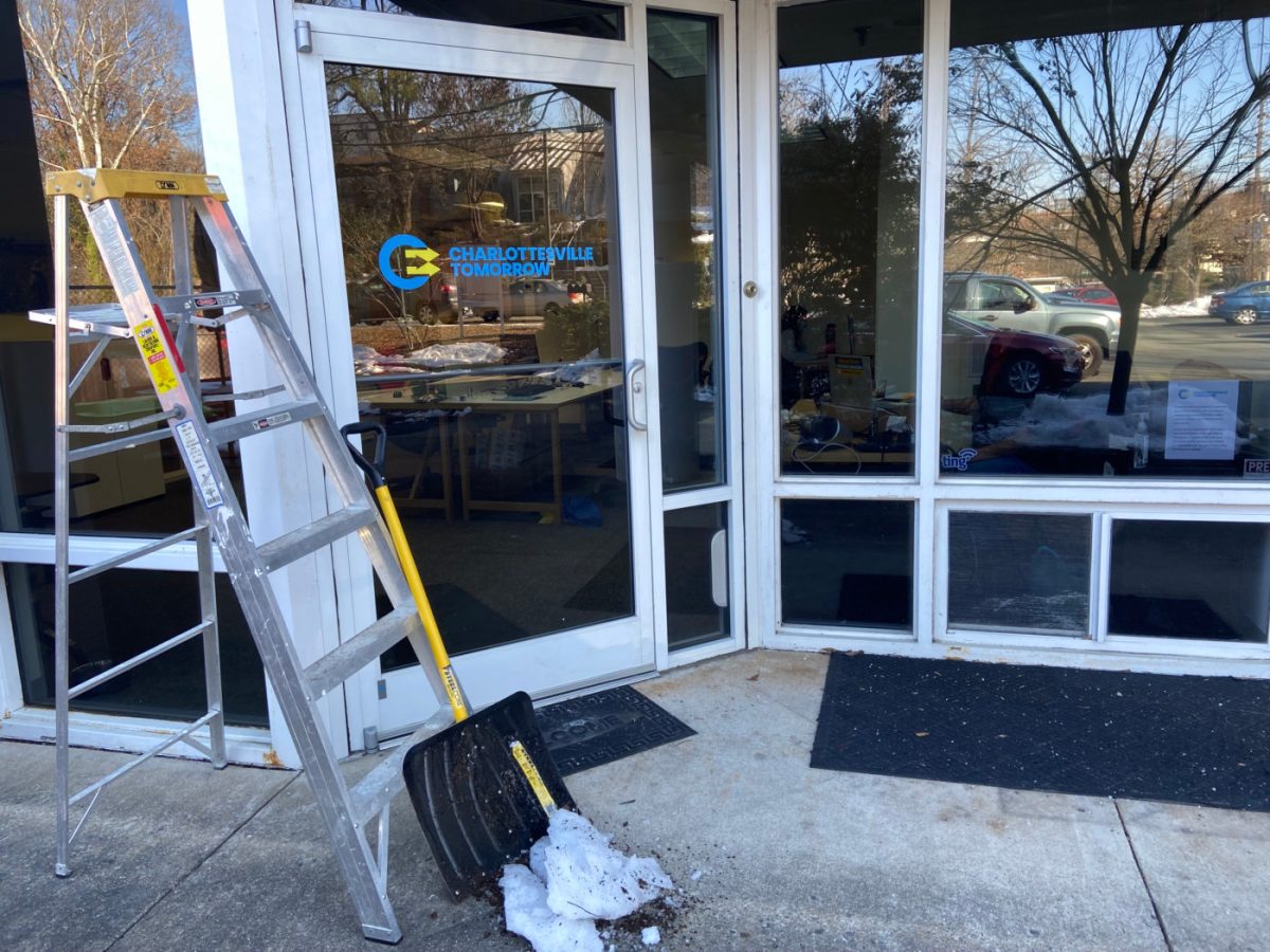 A ladder and shovel, with a bit of snow, sits in front of a glass storefront. The door has the Charlottesville Tomorrow logo on it.