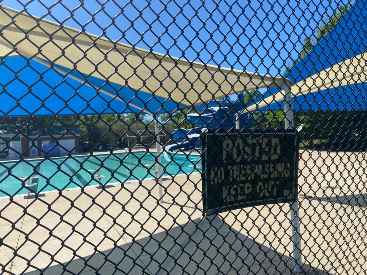 A pool behind a chain link fence with a sign “Posted no trespassing keep out” in the foreground
