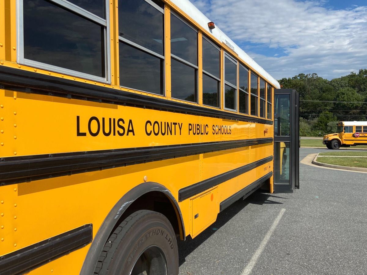 A yellow school bus with the words “Louisa County Public Schools” with another bus in the background.