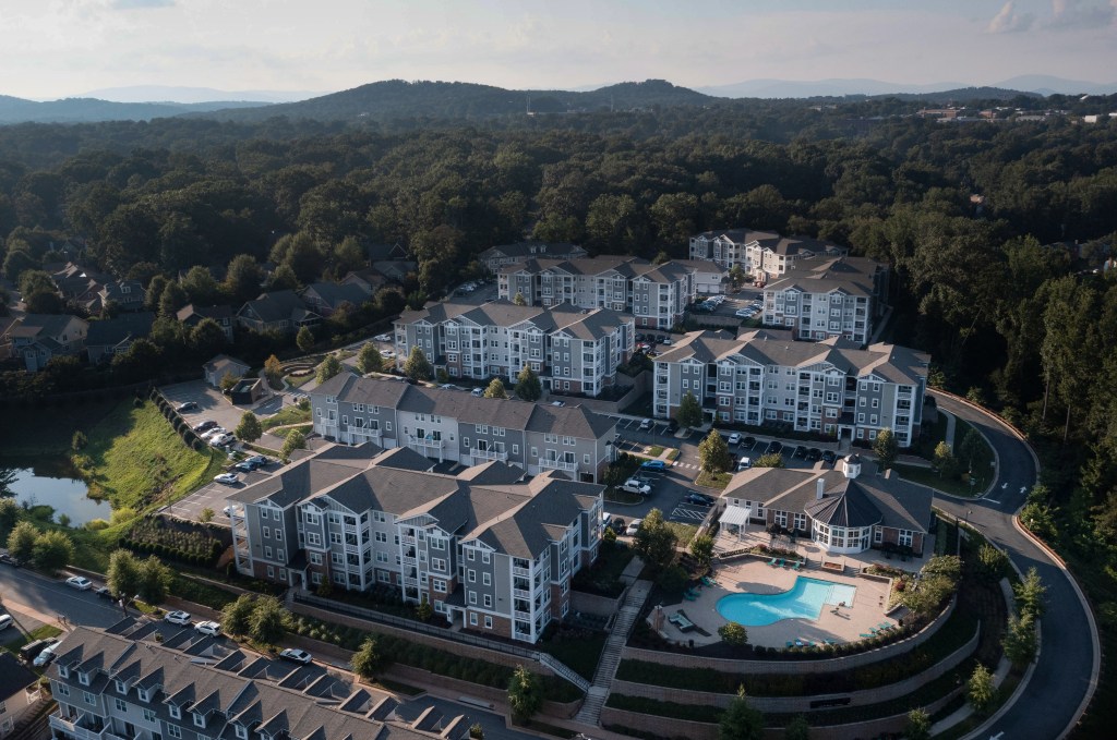 An aerial view of an a multi-building apartment complex, with a pool in the corner