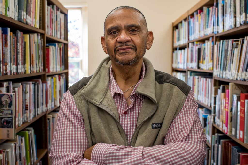 Man in vest stands between two shelves of books, looking at camera