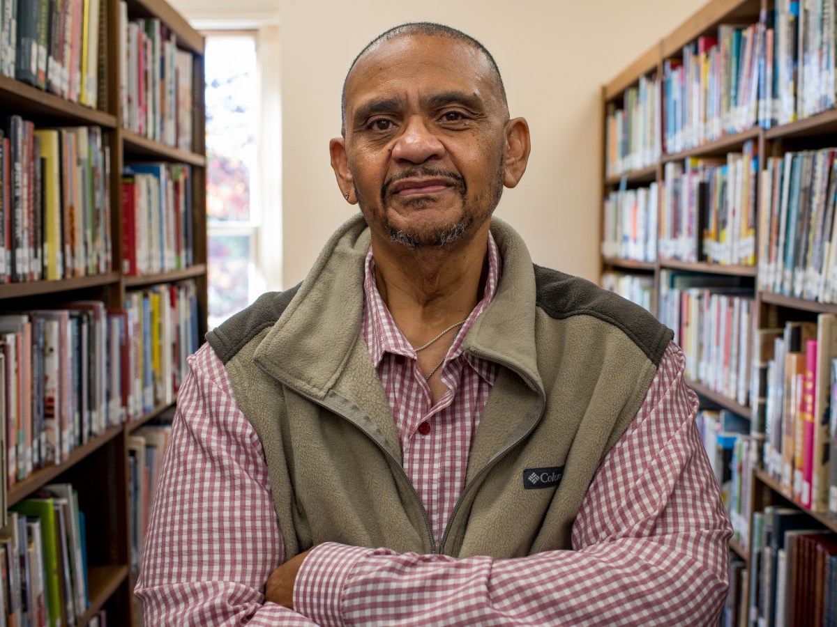 Man in vest stands between two shelves of books, looking at camera