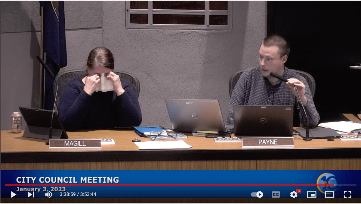 Screenshot of YouTube player showing a woman with the nameplate Magill at a table with a handkerchief to her face, and a man with the nameplate Payne speaking in a microphone. The text reads, "City Council Meeting January 3, 2023."