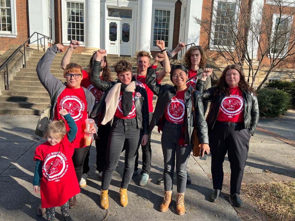 A group of seven adults and one child in matching red T-shirts stand with their fists in the air in front of a brick building with white columns.