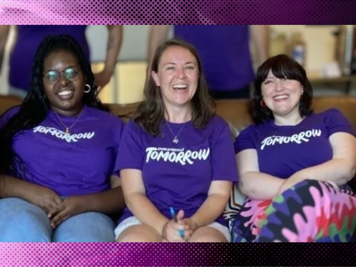 Three people sitting and smiling for camera, all wearing purple t-shirts with the Charlottesville Tomorrow logo.