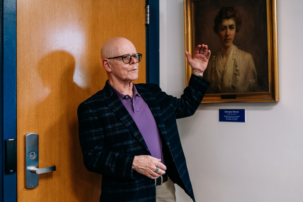 A man stands beside the historic looking portrait of a woman.