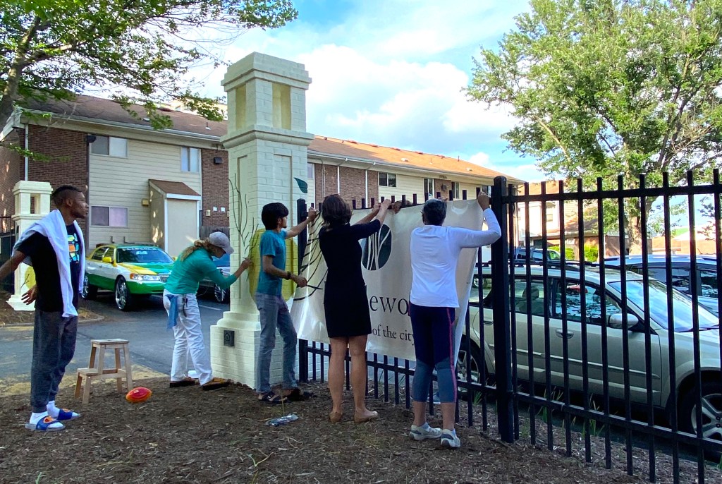 Five young people pin a large sign to a fence in front of apartment buildings.