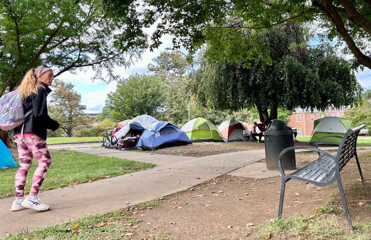 A woman with a backpack walks down a path in a park next to several dome tents.
