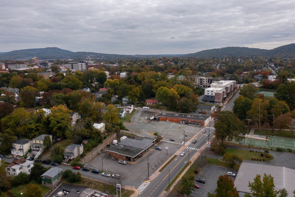 An aerial photo of a vacant lot surrounded by houses and trees, taken in the fall. At the center of the photo is an empty parking lot and a building in bad shape.