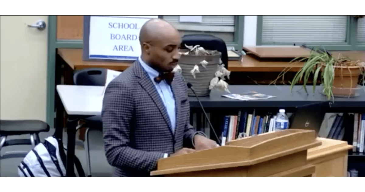 A man stands at a podium speaking to people off camera.