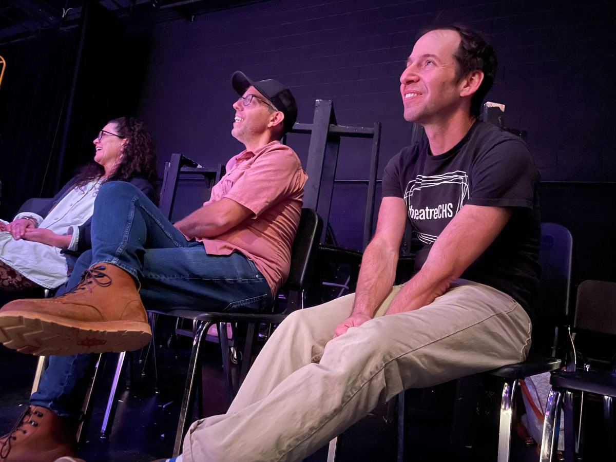 Three people sit in chairs smiling at something off camera.