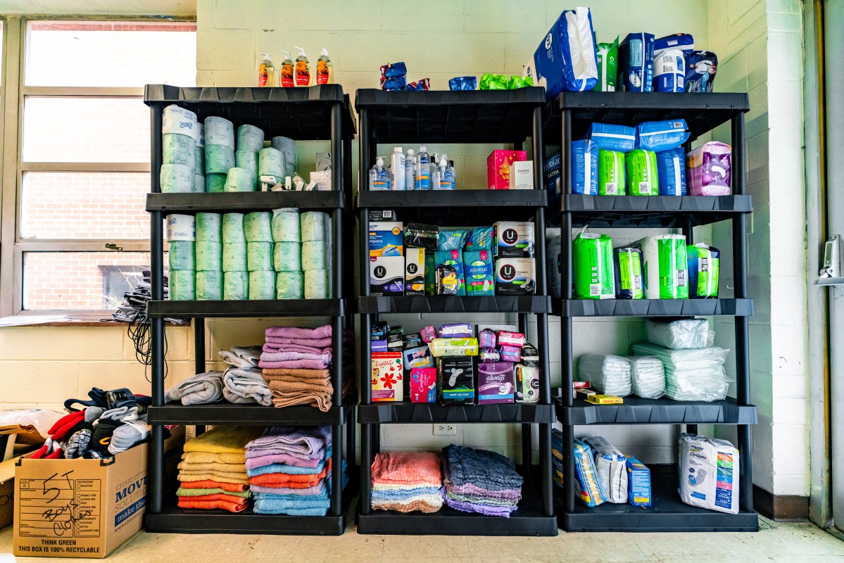 Three black shelves hold various essential items, such as towels, toilet paper, diapers, and feminine hygiene products.