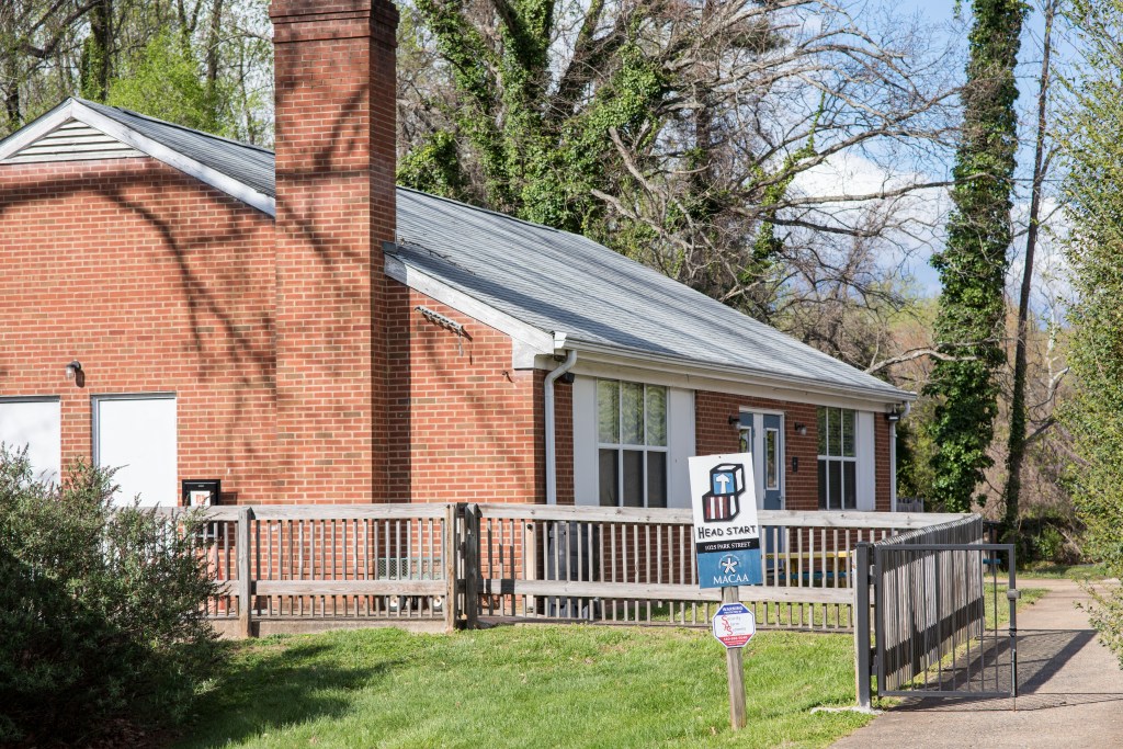 A brick building is surrounded by trees. In front of the building is a small sign that reads "Head Start: MACAA."