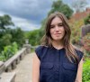 Woman in blue blouse in front of bridge and trees