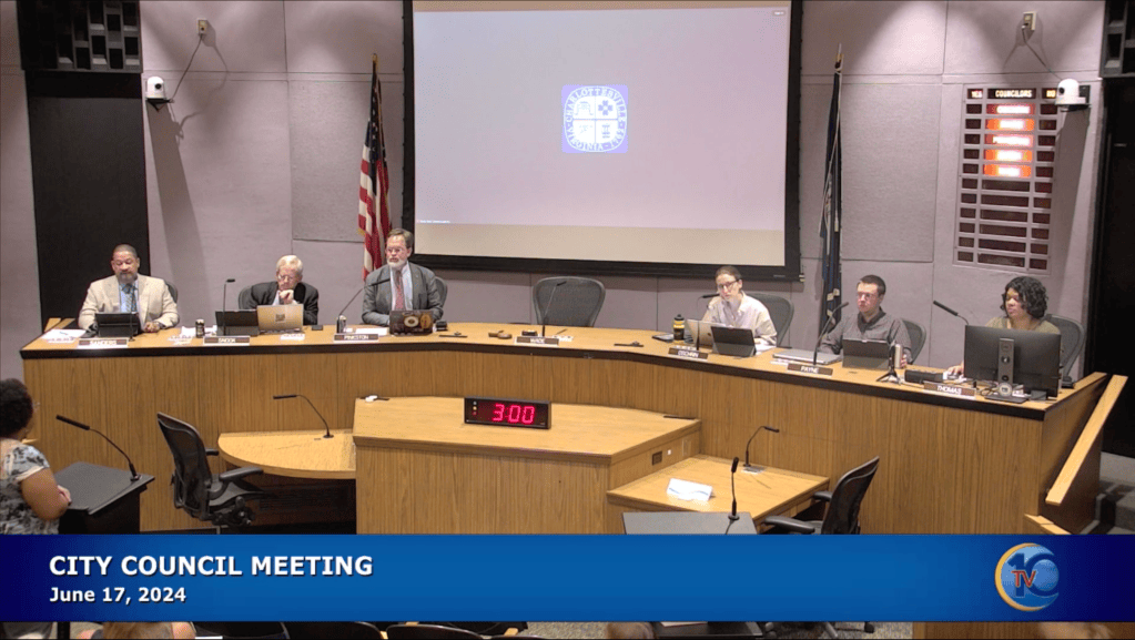 A screenshot of people at a dais with microphones and laptops. Text reads "City Council Meeting June 17, 2024."