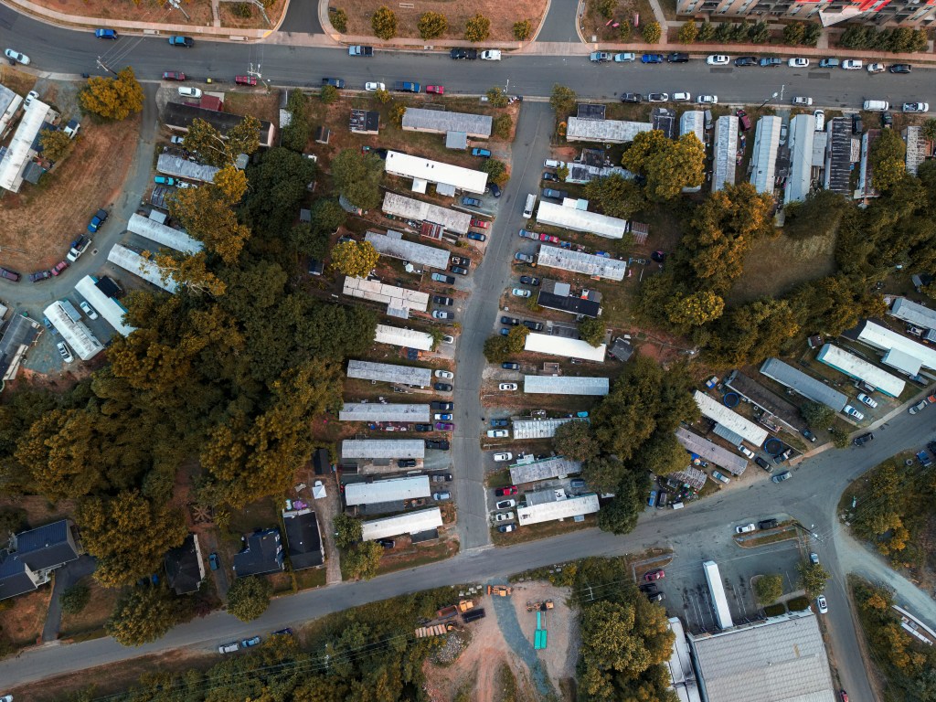 An aerial view of a mobile home park with trees between the rows of trailers.