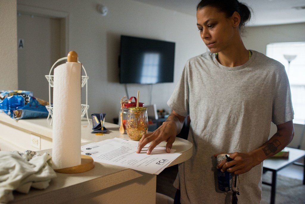 A woman stands at a high counter top looking at a piece of paper. She has a concerned look on her face.