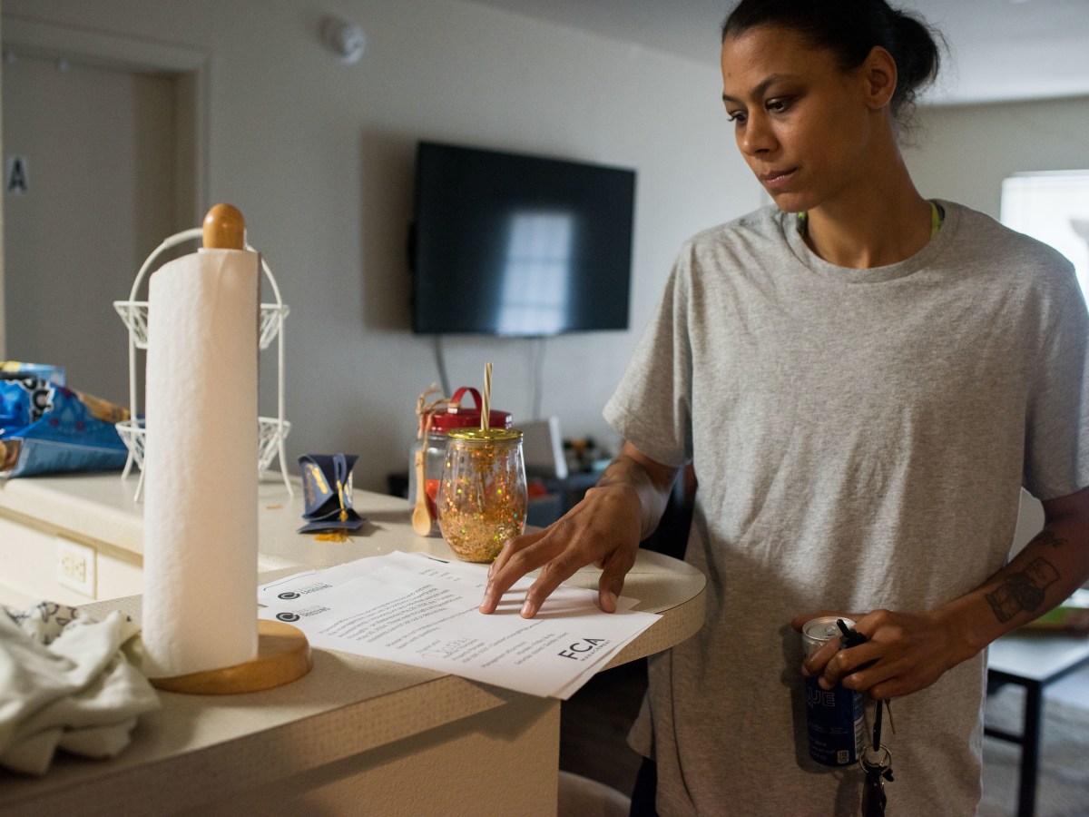 A woman stands at a high counter top looking at a piece of paper. She has a concerned look on her face.
