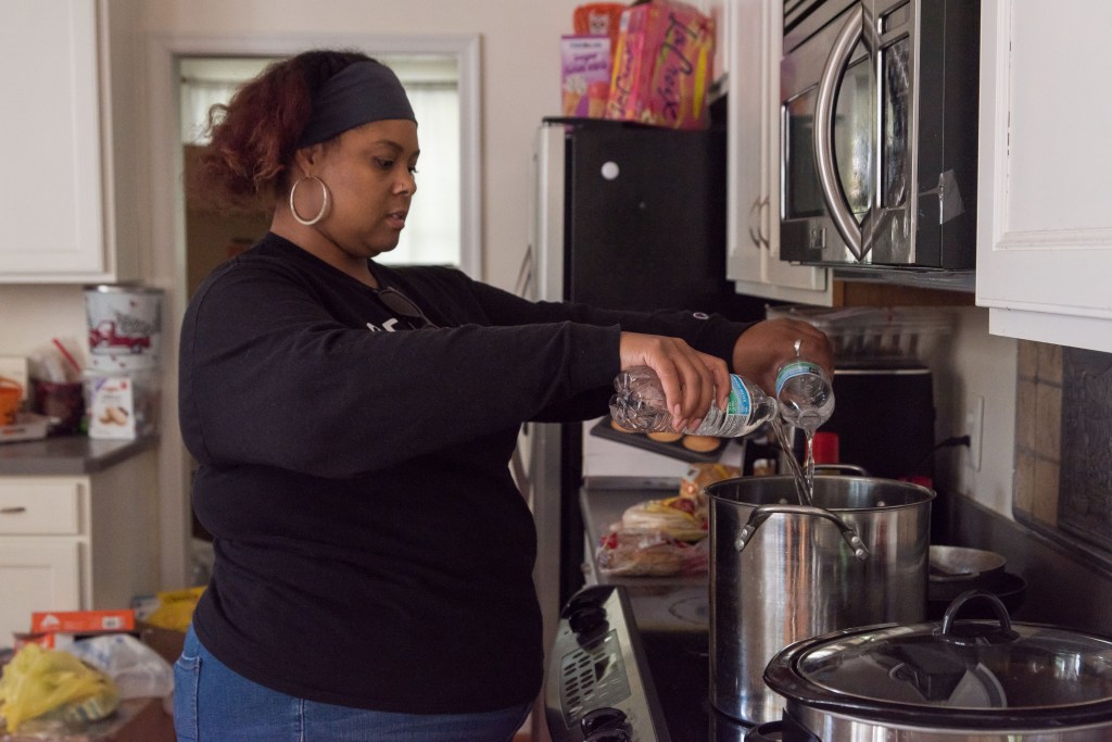 A woman pours bottled water into a stockpot sitting on a stove.