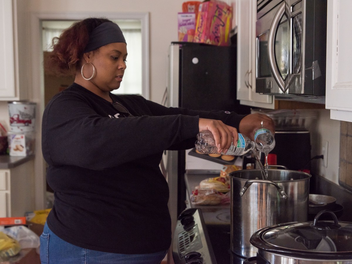 A woman pours bottled water into a stockpot sitting on a stove.