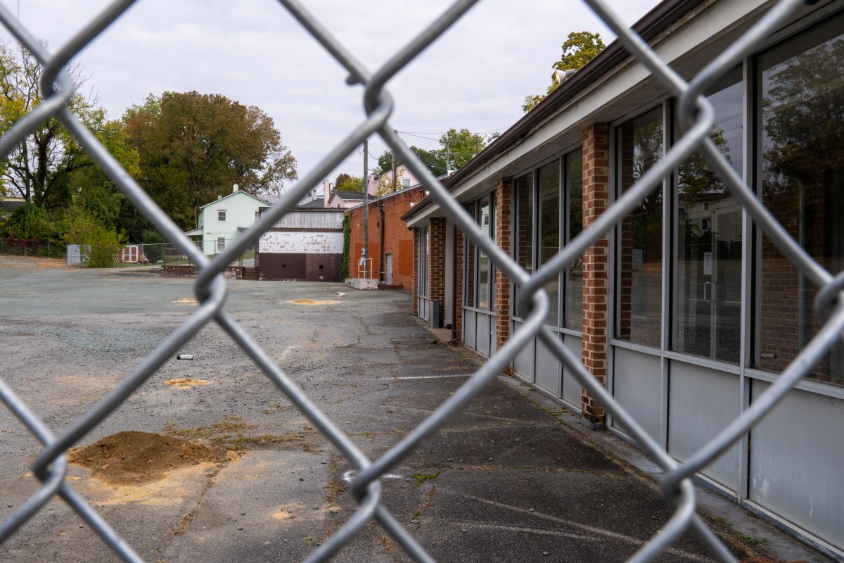 A vacant building that is pictured behind a chainlink fence.