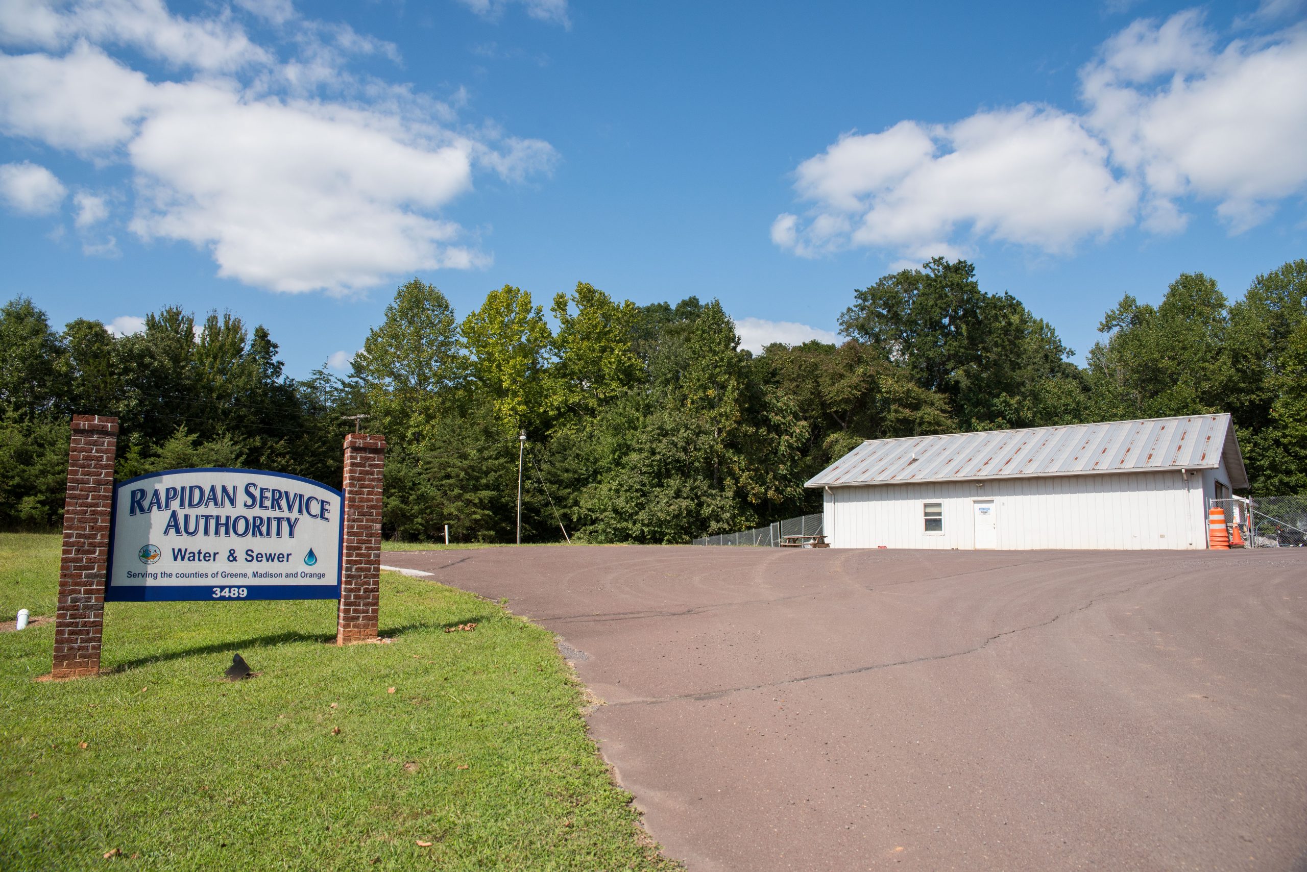 A paved lot is pictured with an aging white shed in the background and a sign that reads, "Rapidan Water Authority" in the grass beside it.