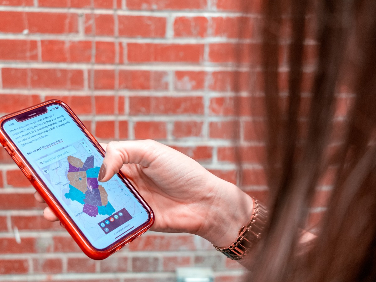 Person holding a smartphone with a colorful map displayed on the screen, standing in front of a brick wall.