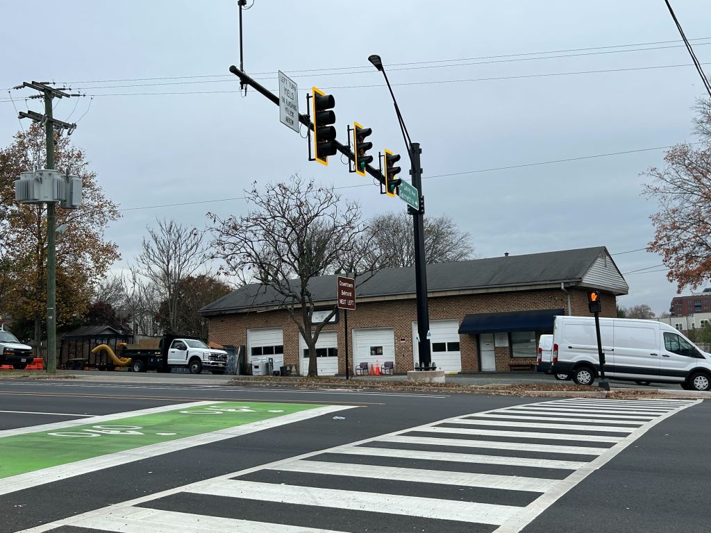 A building with white garage doors sits behind an intersection with a stoplight and a crosswalk.