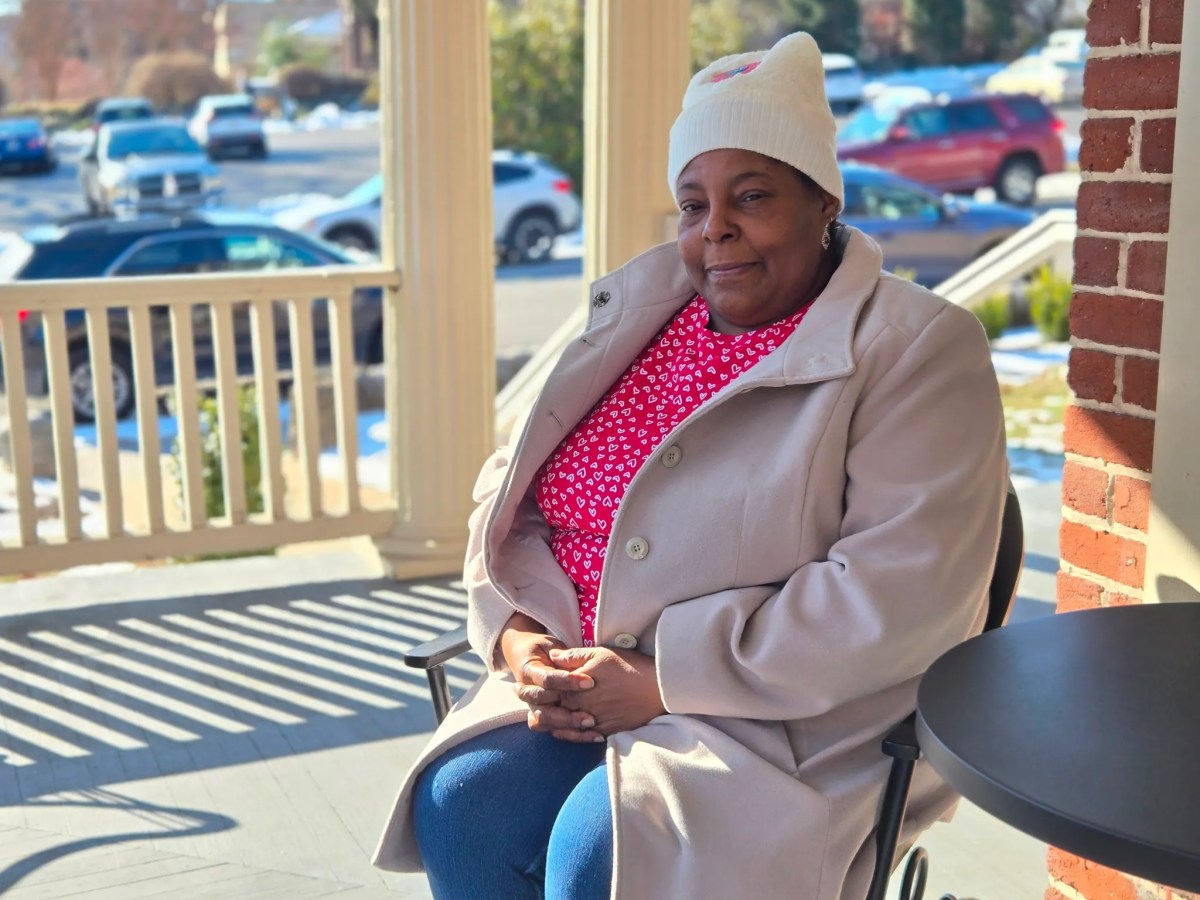 A woman sits on a porch looking at the camera.