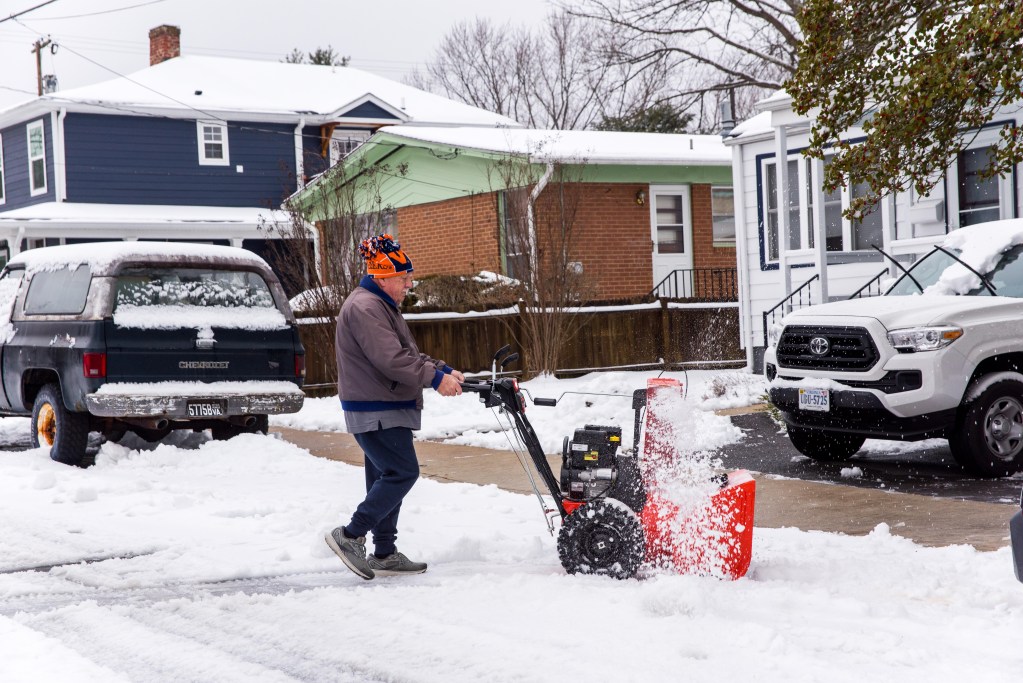 A person pushes a snowblower on a residential street.