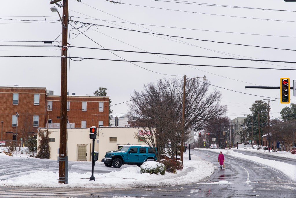 A person walks down the middle of a road, with a traffic light in the foreground.