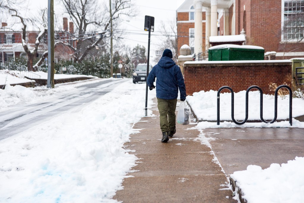 A person walks down a snowy street carrying a plastic bag, brick buildings to the side.